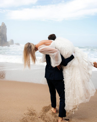Mann trägt Frau auf Schulter am Meeresstrand
